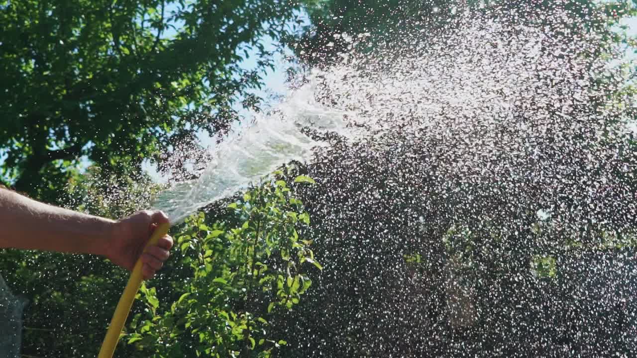 Stream of water spraying from garden hose close-up. Watering the green grass. Slow motion.