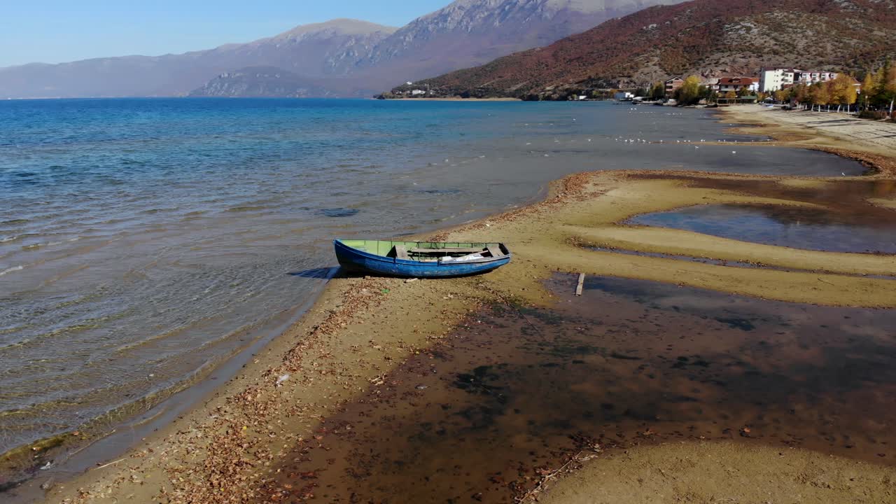 Fishing boat on shore of calm lake of Ohrid with clear blue water and mountains background