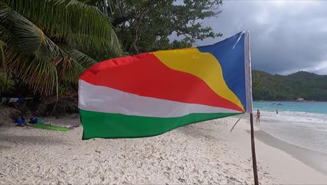 seychelles flag blowing on beach with palm trees and ocean