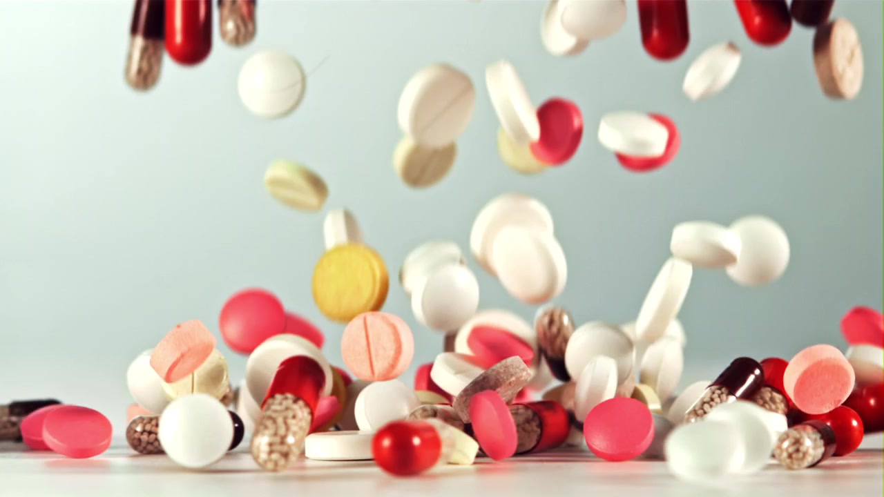 Diverses pilules et gélules pharmaceutiques tombant sur un fond blanc.