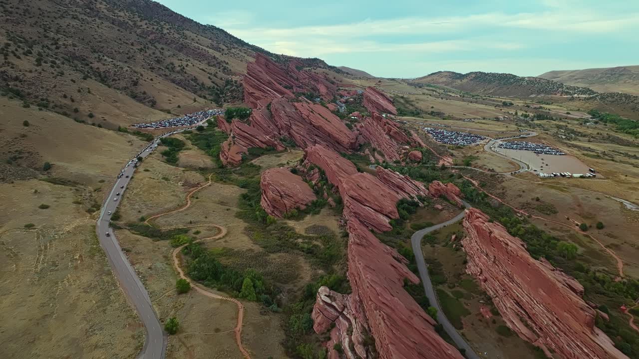 Drone pullback from Red Rocks Amphitheatre showing surrounding cliffs and open terrain under soft afternoon light