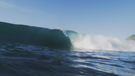 slow-motion shot of a wave crashing with great intensity, filmed from inside the water at sunrise, showcasing the wave's raw power and motion