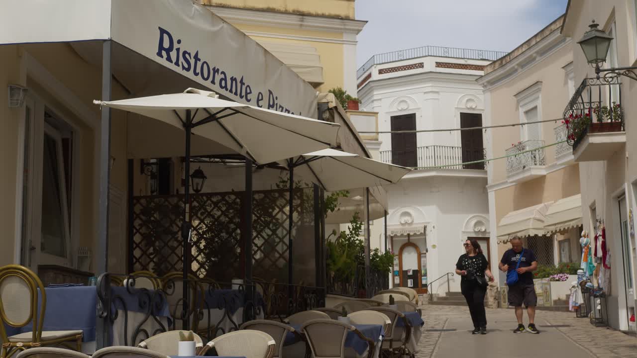 An elderly couple seeking information from a waiter at a local restaurant in Anacapri, surrounded by traditional white architecture, Capri, Italy