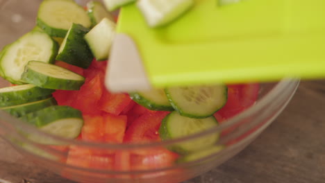 Fresh-sliced-cucumbers-being-placed-into-bowl-of-diced-tomatoes-from-chopping-board