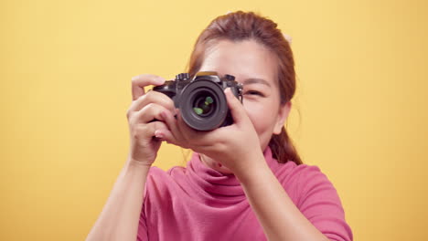 광고를 위한 카피 공간이 있는 디지털 카메라를 사용하여 고립된 노란색 배경 위에 촬영된 스튜디오에 있는 아시아의 멋진 젊은 여성