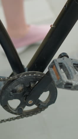 primer plano de una persona con zapatillas rosadas paseando en bicicleta por un camino pavimentado, capturando el pedal de la bicicleta, la cadena y el detalle del neumático trasero, transmitiendo movimiento al aire libre y un ambiente de verano relajado en un entorno urbano