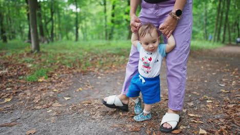 mom's holding her baby's hands helping him to walk. little child learning to walk outdoors. nature backdrop.