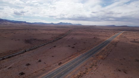 Drohnenaufnahme-Einer-Eisenbahn-Und-Autobahn-In-Der-Wüste-Mit-Einem-Auto-Auf-Der-Straße