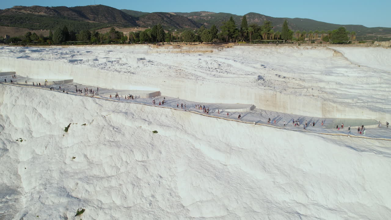Türkiye, Pamukkale'yi ve termal kaplıca sularıyla ünlü travertenleri ve havuzları ziyaret eden insanların havadan görünümü.