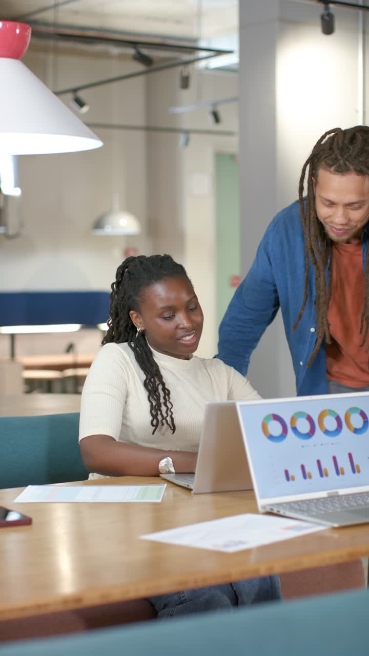 Vertical video: Coworkers at office, woman showing charts, man leaning at laptop, analyzing data
