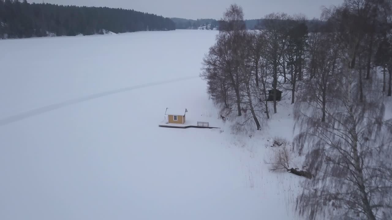 숲 가장자리에 자리잡은 작은 오두막을 부드럽게 확대하면서 광활한 겨울 풍경을 보여주는 항공 영상