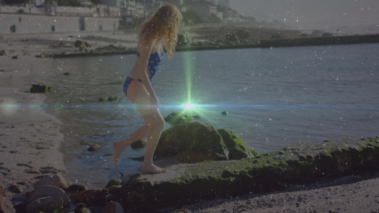 Exploring rocky shoreline, woman in swimsuit with glowing light animation over water