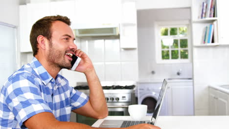 -Hombre-Concentrado-Mirando-La-Computadora-Portátil-Y-Llamando-Por-Teléfono