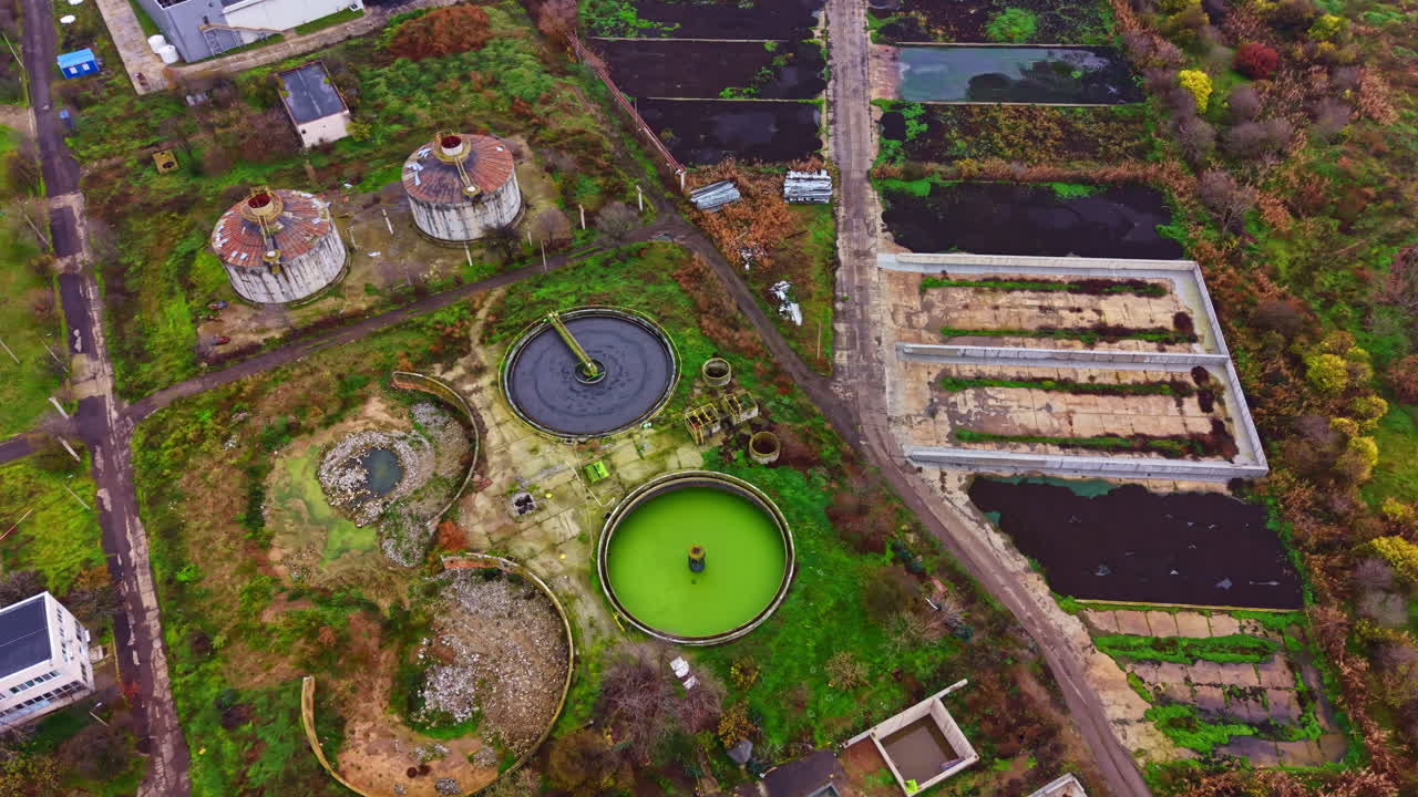 Abandoned industrial site with circular tanks and overgrown land in a desolate area during daytime