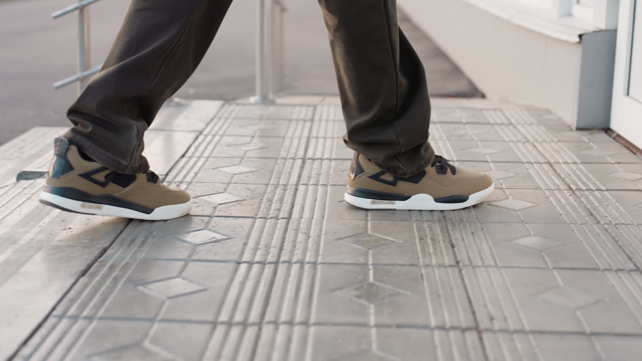Side view of man wearing brown sneakers and dark pants walking on paved surface, mid-step captured in motion, showcasing casual footwear style and dynamic movement in outdoor urban setting