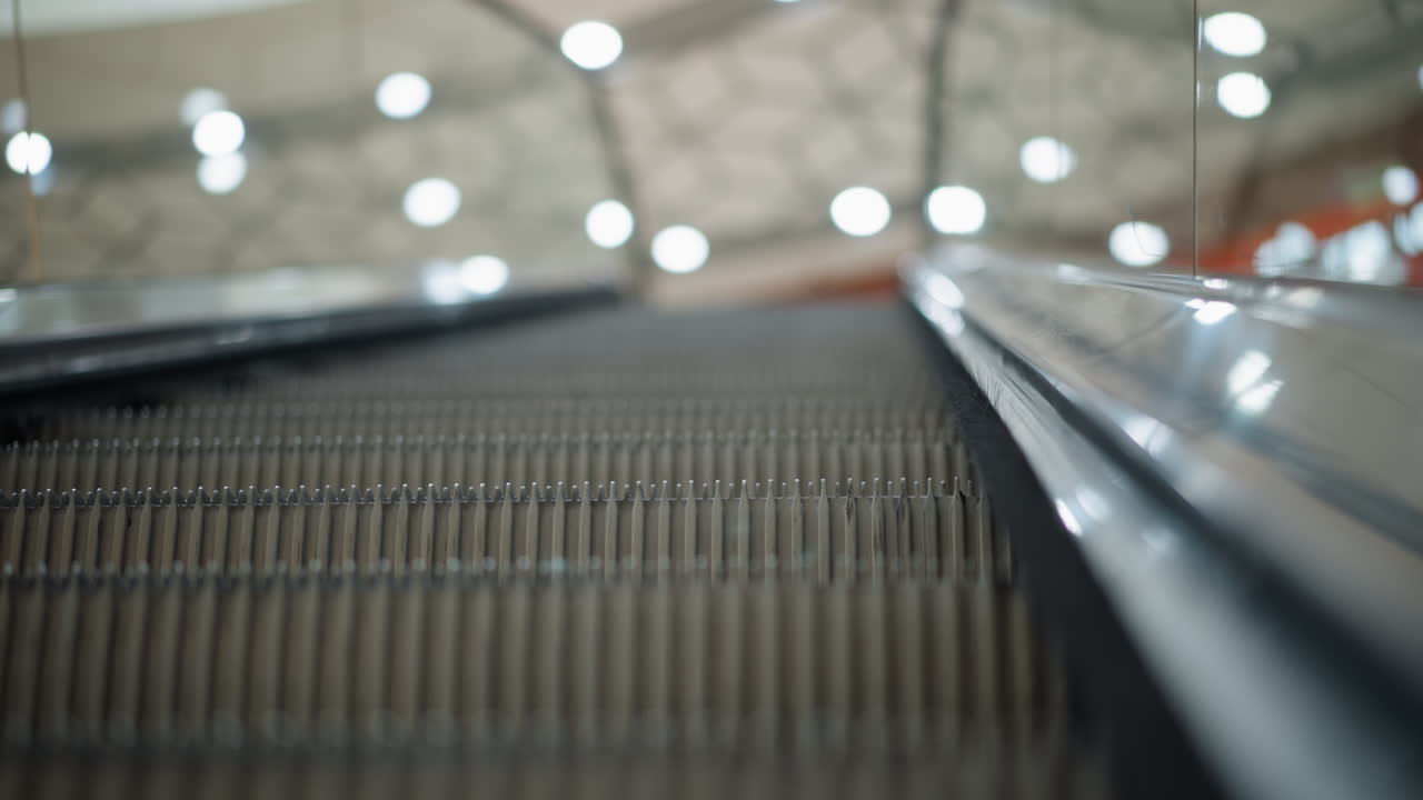 Close-up of moving escalator framed by glass on both sides, capturing the texture and detail of the escalator steps, background features soft bokeh lights