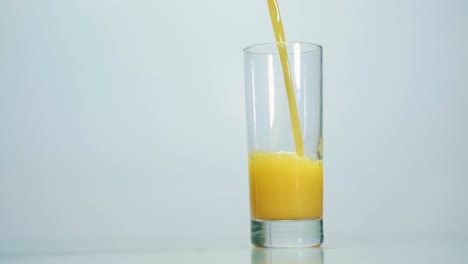 fresh orange juice pouring into clean transparent glass on gray table on white background