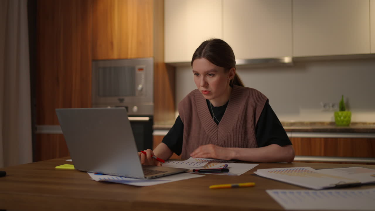 Portrait of a woman working remotely in a home office at a desk with a laptop and notes data on a graph business economist analyst