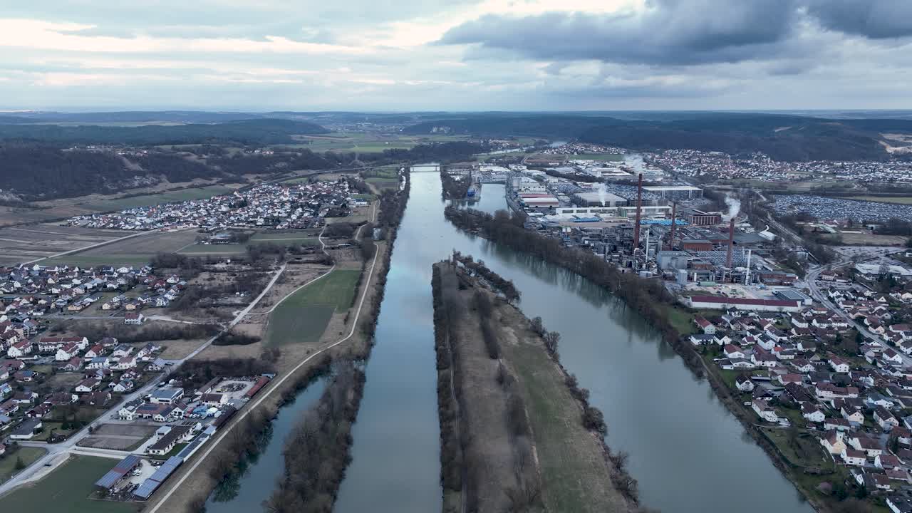 A broad aerial view of the Danube River valley near Kelheim, Germany, showcasing the contrast between a large industrial zone and a peaceful residential area