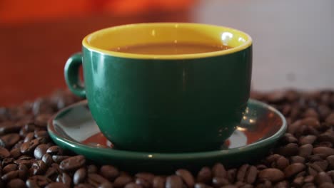 vertiendo leche en una taza de café que está bellamente decorada, parada sobre un montón de granos de café y en una bonita taza de color verde oscuro y claro