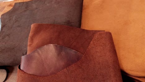 three different rich brown and caramel colours of leather laying on a work bench ready to be processed into leather goods by a small artisan business