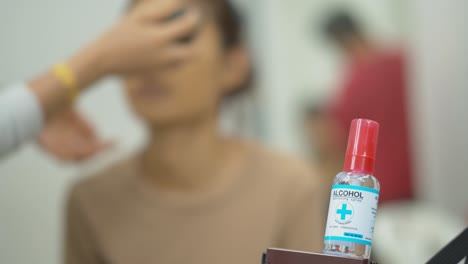 focus pull from an alcohol sanitizer bottle to the model - sanitizer used by the makeup artist before working with the model to prevent spread of virus