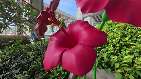 a large hibiscus sculpture with three blooming flowers stands prominently in a public park, adding a vibrant, artistic touch to the surroundings.