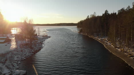 aerial, rising drone shot, of a man standing, at a camp, on a lake shore, surrounded by leafless trees and first snow on the ground, on a sunny, day, near joensuu, north karelia, finland