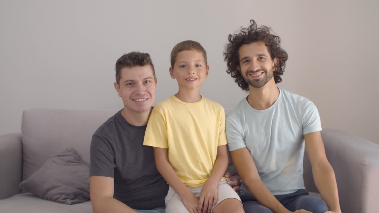 felices y guapos padres gays y un niño posando en casa.