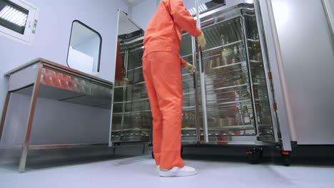 Factory-worker-in-orange-protective-suit-opening-refrigerator-storage