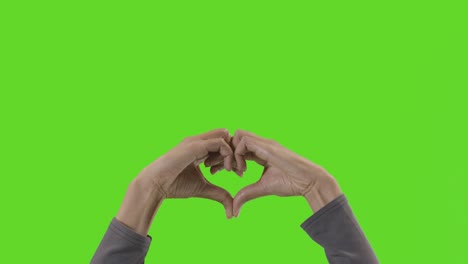 studio close up shot of woman making heart shape symbol for love against green screen