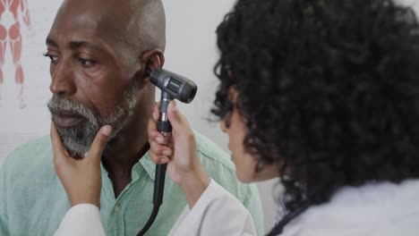 Diverse-female-doctor-examining-male-patient-in-consulting-room,-using-otoscopy,-slow-motion