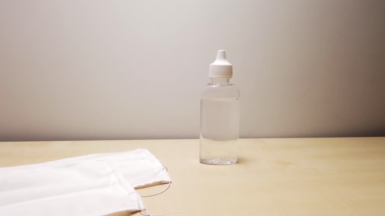 Man's hand taking an antiseptic gel and an medical protective mask from a wooden table. Corona Virus idea