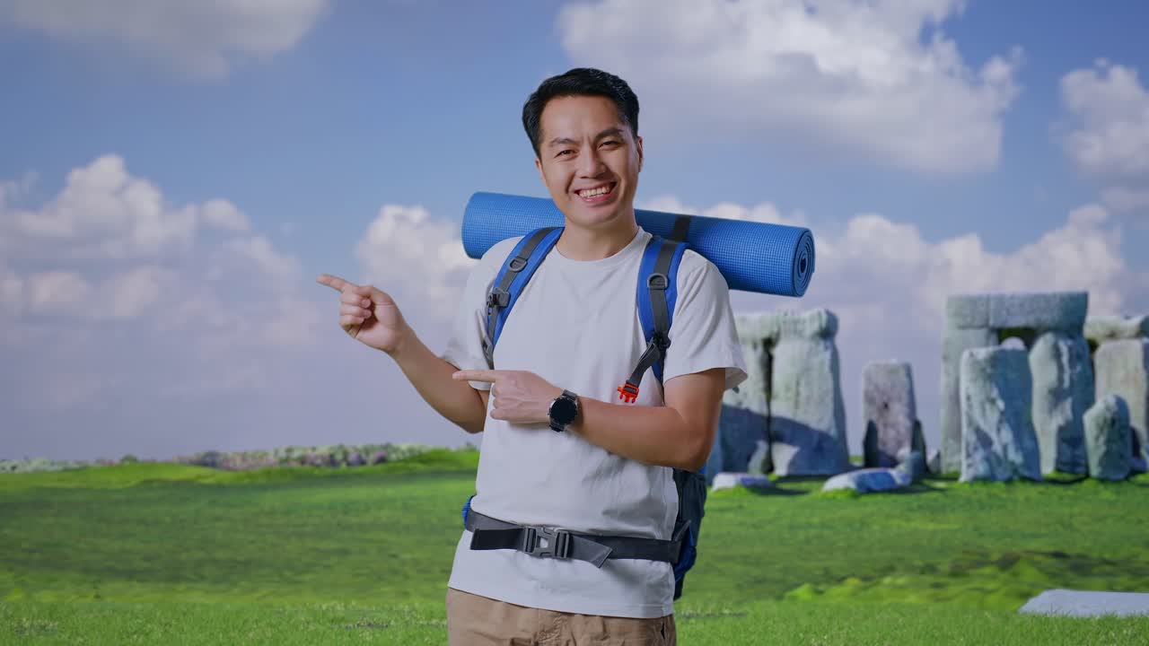 Asian Male Hiker With Mountaineering Backpack Smiling And Pointing To Side While Traveling In Stonehenge