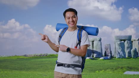asian male hiker with mountaineering backpack smiling and pointing to side while traveling in stonehenge