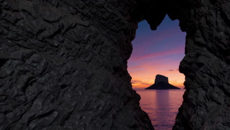 view from a cave opening of a sunset over the sea with a distant island