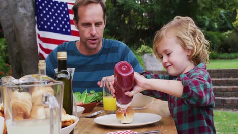 smiling caucasian man watching son using ketchup during celebration meal in garden