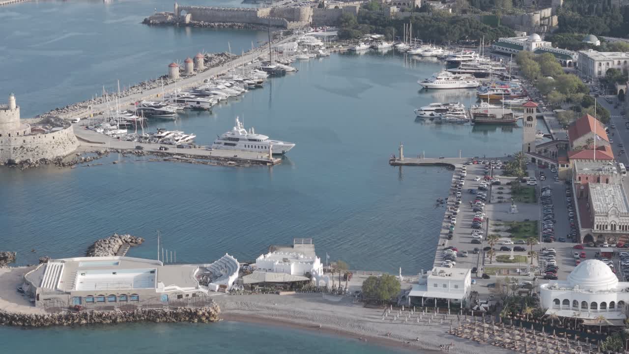 Aerial drone footage of Mandraki Harbor in Rhodes, Greece, showing the historic windmills and boats Captured with cinematic drone techniques.