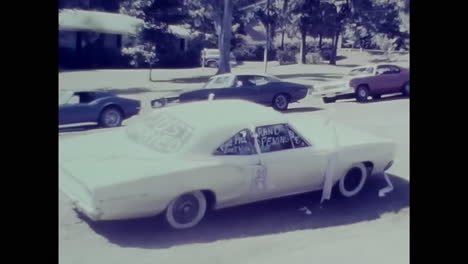 man standing next to white car in parking lot during 1970s in usa. circa usa - 1970s: a man stands next to a white car in a parking lot, captured in this archive video from the 1970s in the usa.