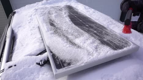 someone brushing snow off of a solar panel that is mounted on top of an suv ¼ speed