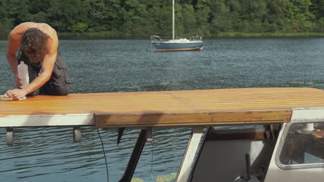 Topless-young-man-uses-acetone-to-wipe-down-sanded-roof-planks-before-varnishing