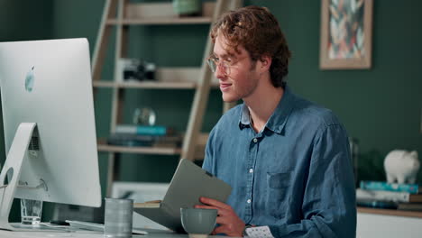man working at a desk with a computer and a book