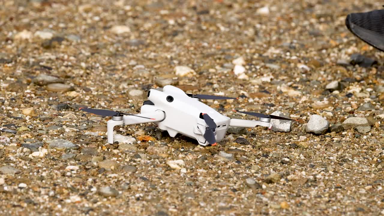 A person retrieves a drone from rocky ground, showcasing careful handling in natural outdoor lighting