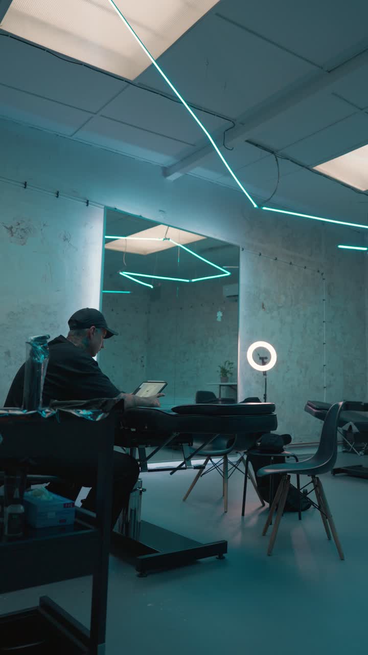 Vertical pan of cool studio, tattoo artist sit and watch tablet on client chair