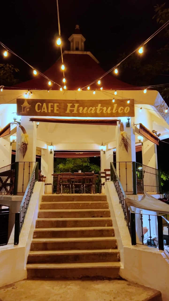 Night view showing Cafe Huatulco entrance with warm string lights, staircase and traditional architecture creating welcoming ambiance in Huatulco, Oaxaca, Mexico at night