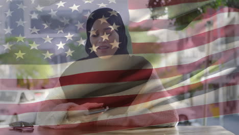 animation of american flag waving over biracial woman in hijab talking on her smartphone