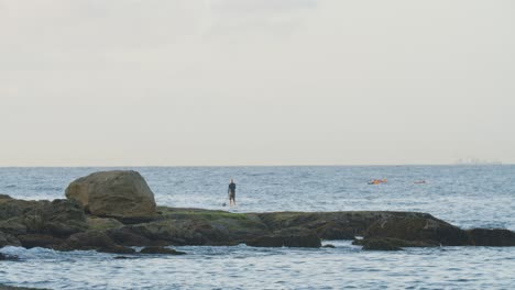 person on paddle board on rocky ocean coast in sydney, australia