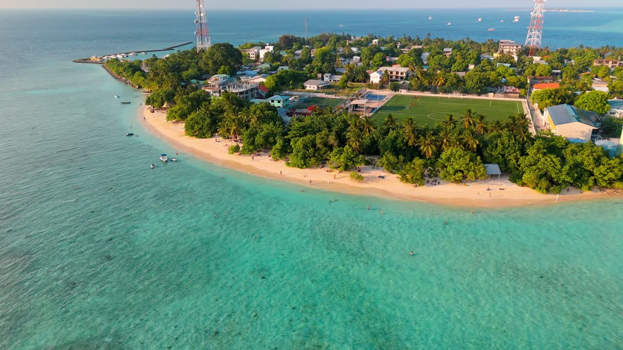 A stunning aerial drone view showcasing Rasdhoo Island surrounded by crystal-clear turquoise waters and vibrant coral reefs in the Maldives.