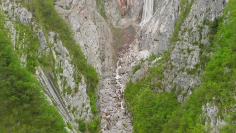 Aerial-footage-of-a-waterfall-and-river-going-through-a-green-and-steep-canyon-in-Slovenia