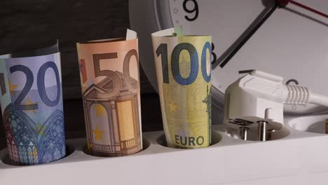 closeup shot of currency on an electrical socket with a clock behind them.